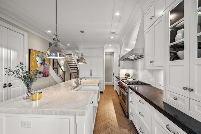 kitchen with an island with sink, parquet floors, white cabinets, range with two ovens, and wall chimney range hood