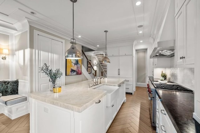 kitchen with light parquet floors, hanging light fixtures, stainless steel range, an island with sink, and white cabinets