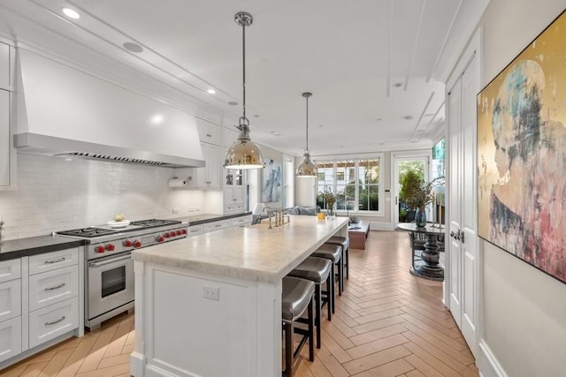 kitchen featuring stainless steel stove, white cabinets, a center island, light parquet flooring, and wall chimney exhaust hood