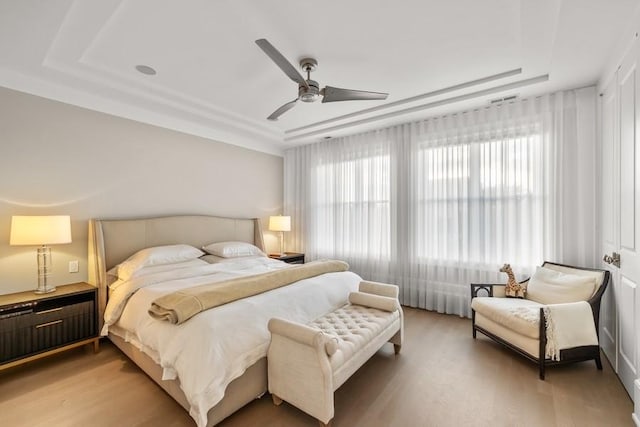 bedroom with ceiling fan, wood-type flooring, and a tray ceiling