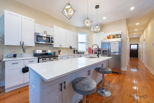 kitchen with sink, stainless steel appliances, white cabinets, hanging light fixtures, and a kitchen island with sink