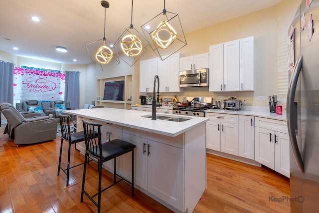 kitchen featuring a kitchen breakfast bar, stainless steel appliances, pendant lighting, white cabinetry, and a kitchen island with sink