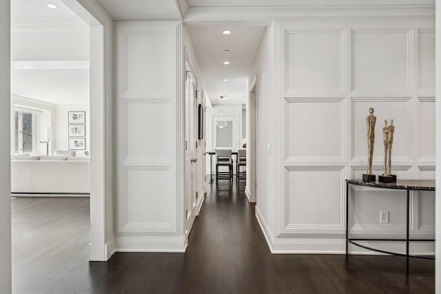 hallway with dark wood-type flooring, recessed lighting, crown molding, and a decorative wall