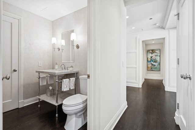 half bathroom with toilet, a sink, baseboards, and wood finished floors