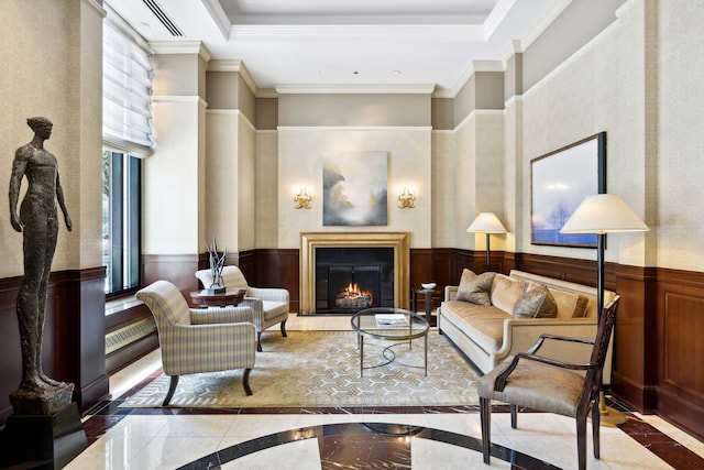 living area featuring a tray ceiling, marble finish floor, a wainscoted wall, ornamental molding, and a warm lit fireplace