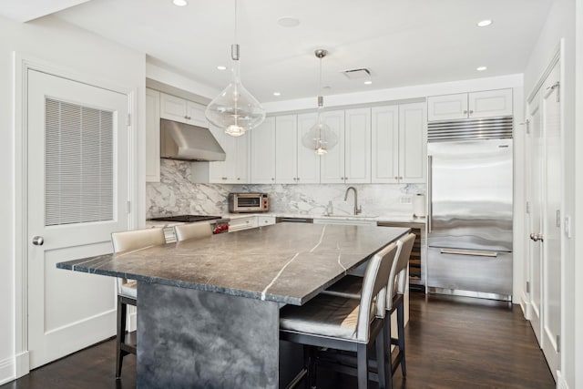 kitchen featuring a breakfast bar area, under cabinet range hood, a sink, appliances with stainless steel finishes, and tasteful backsplash