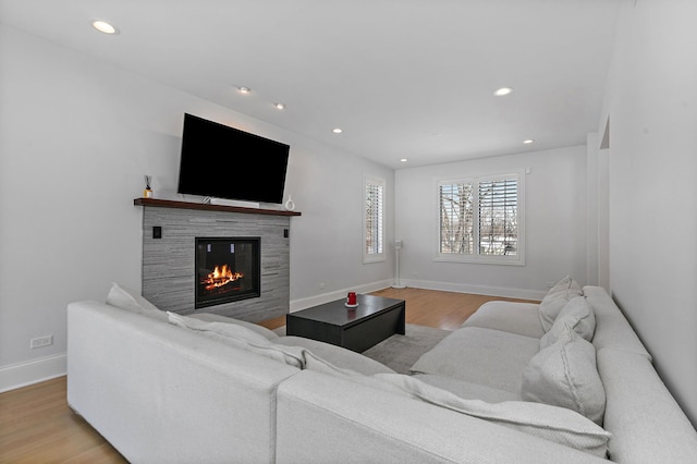 living area featuring baseboards, recessed lighting, a glass covered fireplace, and light wood-style floors