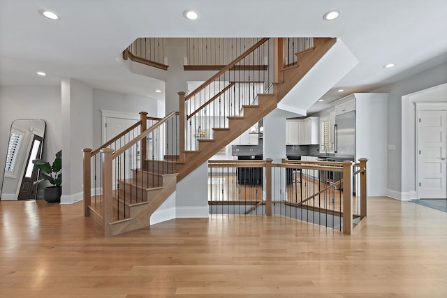 staircase with baseboards, wood finished floors, a towering ceiling, and recessed lighting