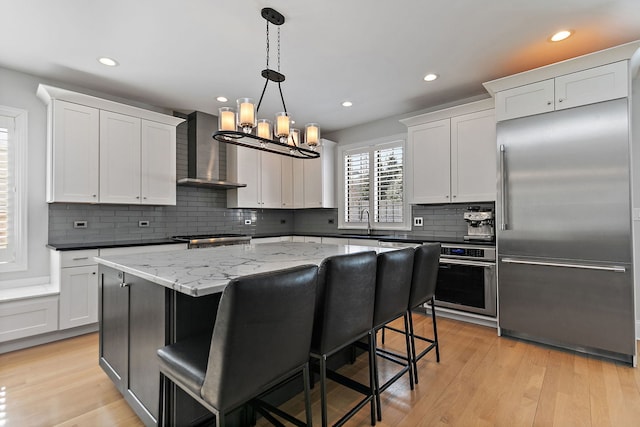 kitchen featuring pendant lighting, appliances with stainless steel finishes, white cabinetry, a kitchen island, and wall chimney range hood