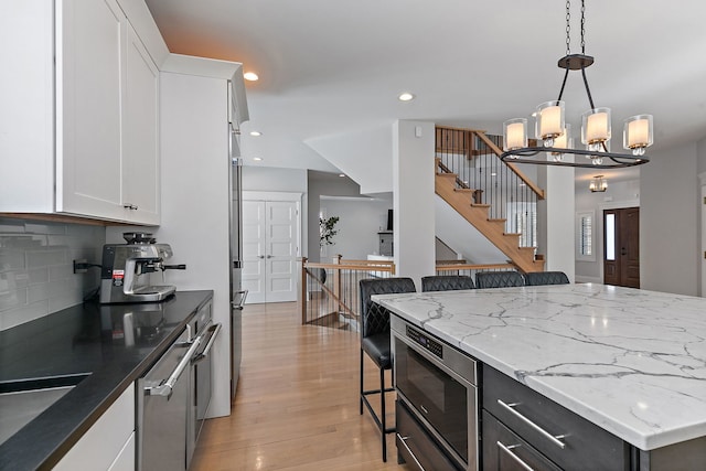 kitchen with white cabinets, a breakfast bar, decorative light fixtures, light wood-type flooring, and recessed lighting