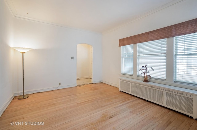 empty room featuring arched walkways, ornamental molding, radiator heating unit, and light wood-style floors