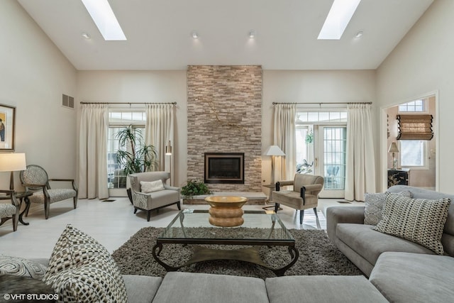 living room featuring visible vents, high vaulted ceiling, a stone fireplace, and a skylight