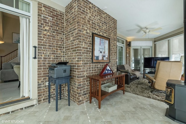 interior space with a wood stove, a ceiling fan, and brick wall