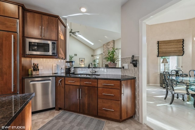 kitchen featuring dark stone countertops, a sink, decorative backsplash, built in appliances, and lofted ceiling with skylight