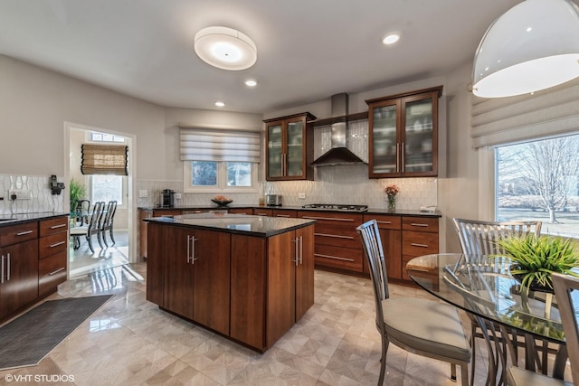 kitchen featuring a center island, glass insert cabinets, wall chimney range hood, decorative backsplash, and recessed lighting