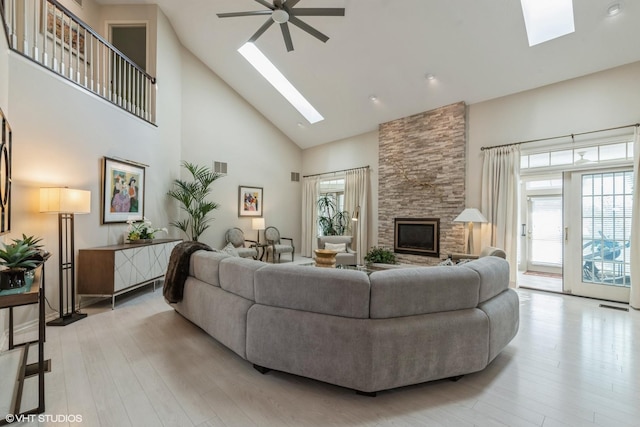 living room with high vaulted ceiling, a skylight, a fireplace, light wood finished floors, and ceiling fan