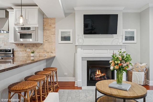 interior space with ornamental molding, baseboards, a tiled fireplace, and wood finished floors