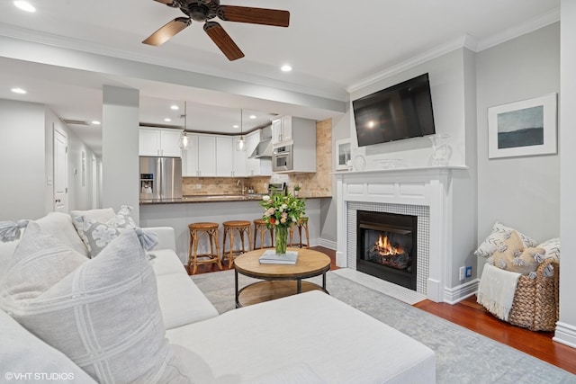 living room with crown molding, dark wood finished floors, recessed lighting, a tiled fireplace, and baseboards