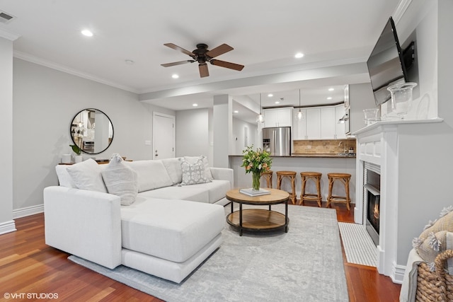 living room with baseboards, a fireplace with flush hearth, wood finished floors, crown molding, and recessed lighting