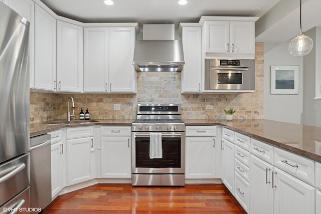 kitchen featuring tasteful backsplash, appliances with stainless steel finishes, a sink, wall chimney range hood, and wood finished floors