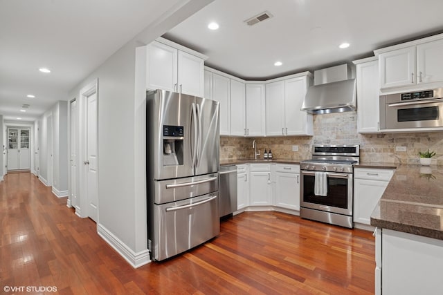 kitchen featuring stainless steel appliances, wall chimney range hood, dark wood finished floors, and visible vents