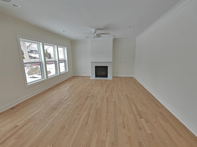 unfurnished living room with ceiling fan, ornamental molding, a tiled fireplace, and light hardwood / wood-style floors