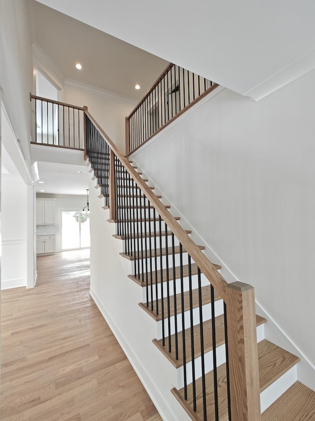 stairs with ornamental molding, a towering ceiling, hardwood / wood-style floors, and a chandelier