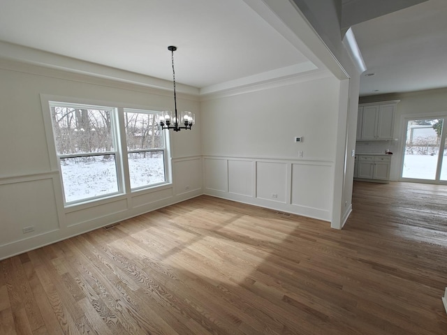 unfurnished dining area with an inviting chandelier, hardwood / wood-style floors, and a raised ceiling