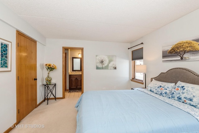 bedroom featuring baseboards, ensuite bathroom, a textured ceiling, and light colored carpet