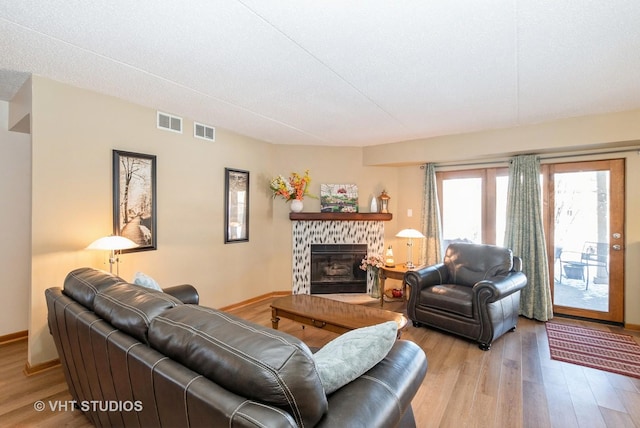 living area featuring a stone fireplace, wood finished floors, and visible vents