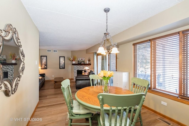 dining room with visible vents, a stone fireplace, light wood-style flooring, and baseboards