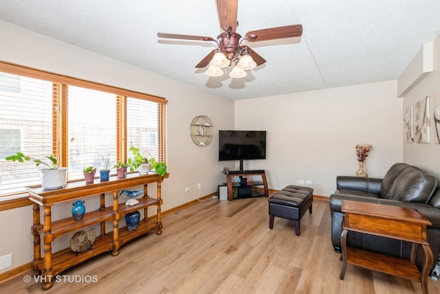 living room with a ceiling fan, light wood-style flooring, baseboards, and a textured ceiling