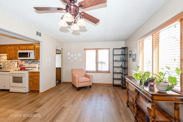 living area featuring a ceiling fan, visible vents, light wood-style flooring, and baseboards