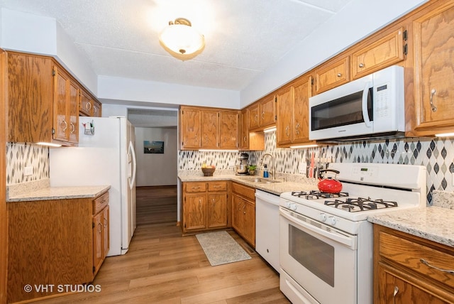 kitchen featuring white appliances, decorative backsplash, brown cabinetry, light wood-style floors, and a sink