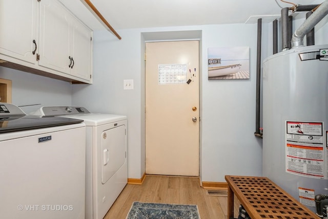 clothes washing area with light wood-style floors, washing machine and dryer, water heater, and cabinet space