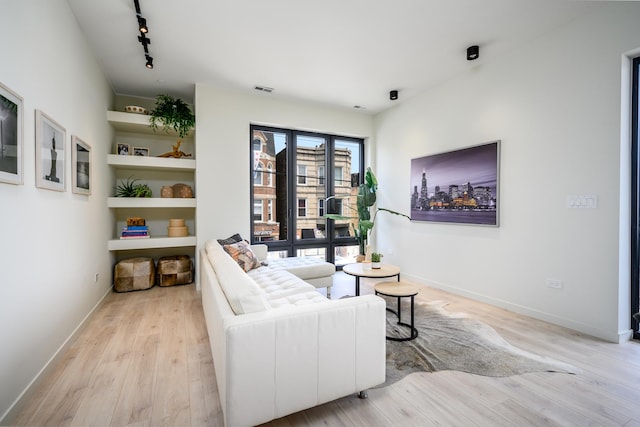 living room with baseboards, light wood finished floors, visible vents, and track lighting