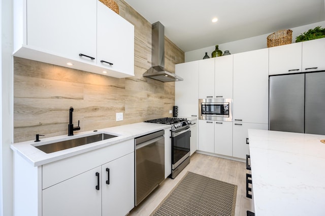 kitchen featuring wall chimney exhaust hood, appliances with stainless steel finishes, light stone counters, white cabinetry, and a sink