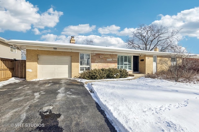 ranch-style home featuring aphalt driveway, brick siding, a chimney, and an attached garage