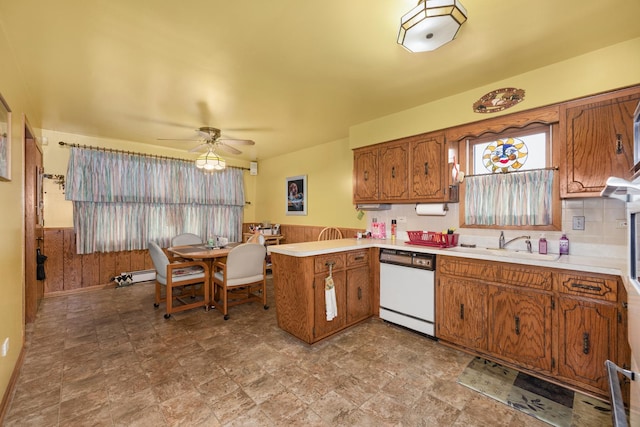 kitchen with white dishwasher, a peninsula, light countertops, wainscoting, and brown cabinetry