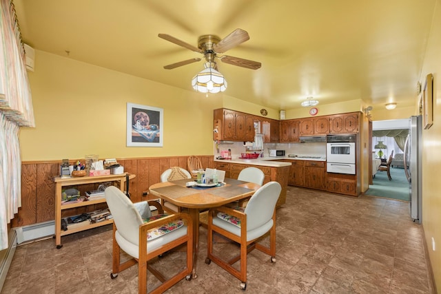 dining area with a ceiling fan, wainscoting, and wood walls