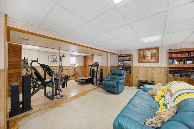 living area with a paneled ceiling, wooden walls, and wainscoting