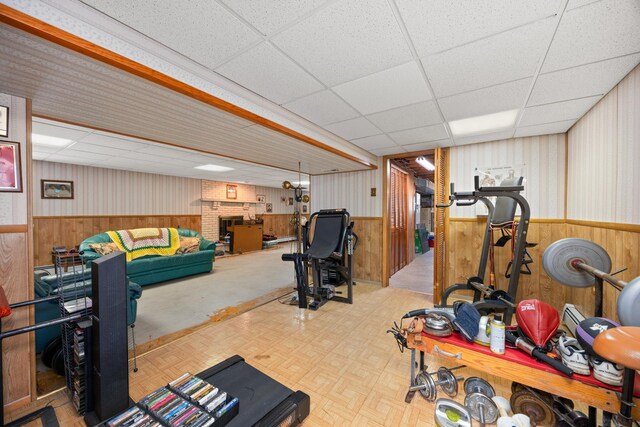 exercise area featuring a wainscoted wall, a brick fireplace, a drop ceiling, and wooden walls