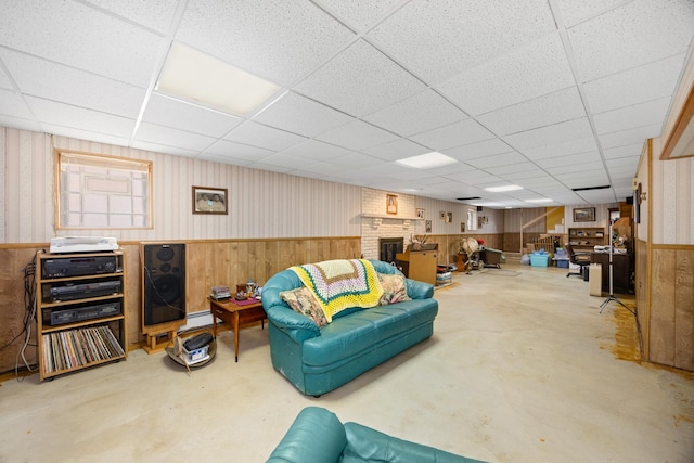 living room with concrete flooring, a brick fireplace, wainscoting, and a drop ceiling