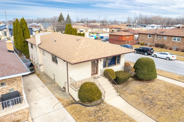 exterior space featuring a residential view, brick siding, driveway, and roof with shingles