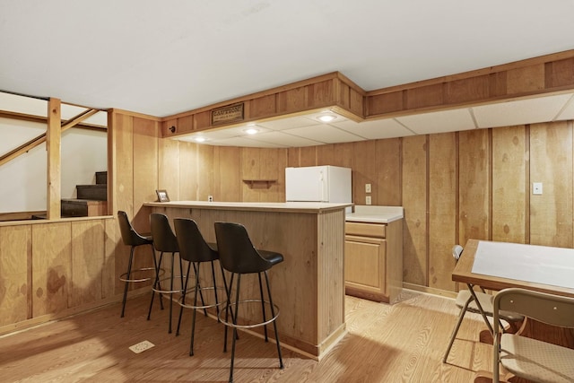 kitchen with kitchen peninsula, light hardwood / wood-style flooring, white fridge, a kitchen bar, and wooden walls