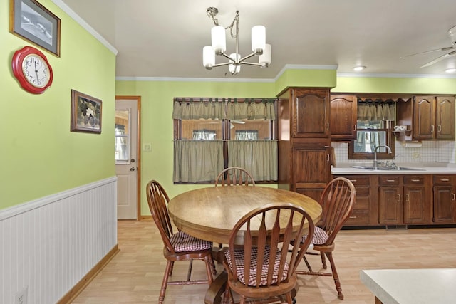 dining space with ceiling fan with notable chandelier, light hardwood / wood-style flooring, sink, and crown molding