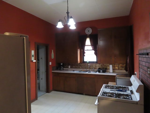 kitchen featuring hanging light fixtures, a notable chandelier, white gas stove, stainless steel fridge, and sink