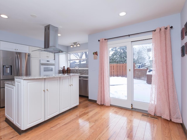 kitchen with white cabinetry, a kitchen island, light stone counters, appliances with stainless steel finishes, and island exhaust hood