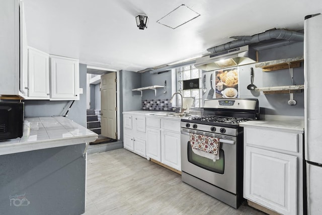 kitchen with sink, stainless steel gas range oven, light hardwood / wood-style floors, decorative backsplash, and white cabinets