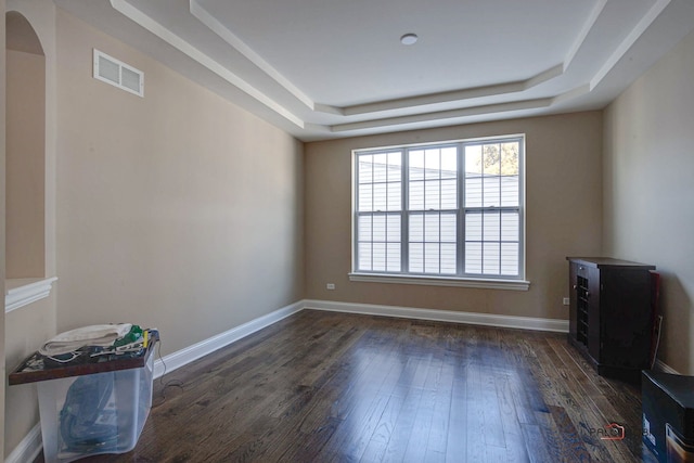 spare room with a tray ceiling, visible vents, dark wood finished floors, and arched walkways